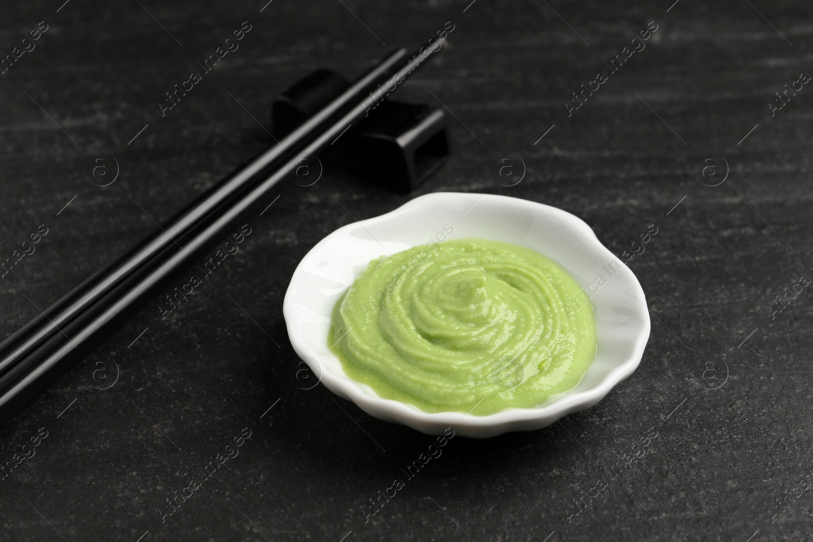 Photo of Hot wasabi paste and chopsticks on dark textured table, closeup