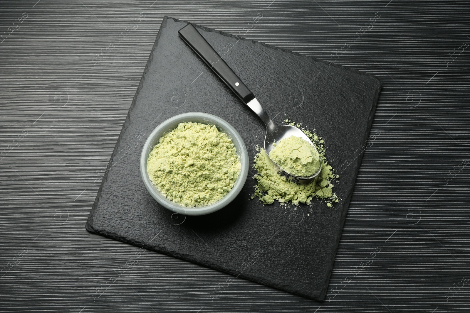 Photo of Dry wasabi powder and spoon on black textured table, top view