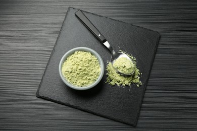 Photo of Dry wasabi powder and spoon on black textured table, top view