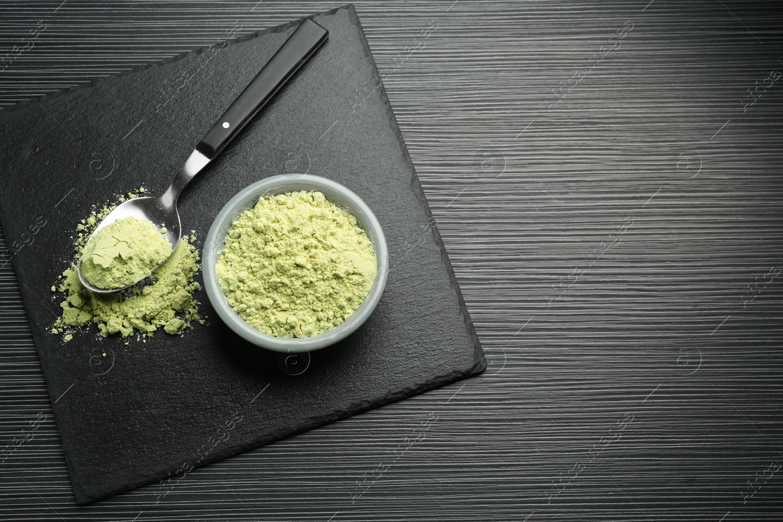 Photo of Dry wasabi powder and spoon on black textured table, top view. Space for text