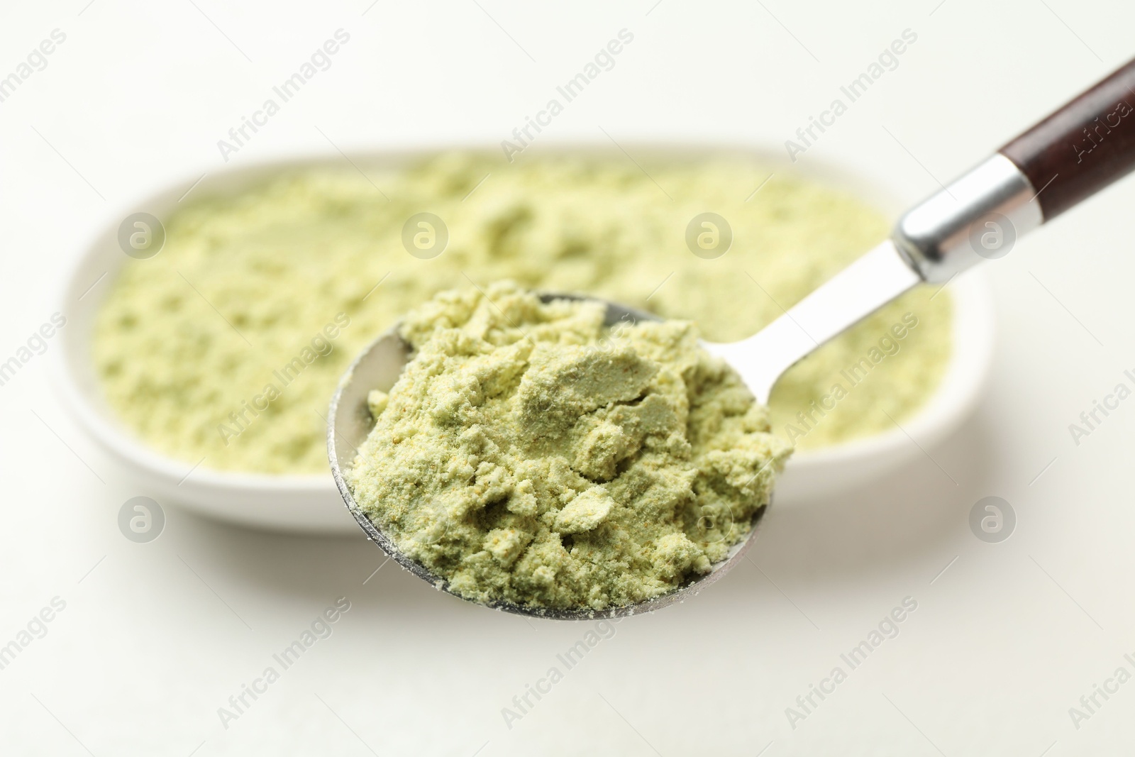 Photo of Spoon with dry wasabi powder on blurred background, closeup