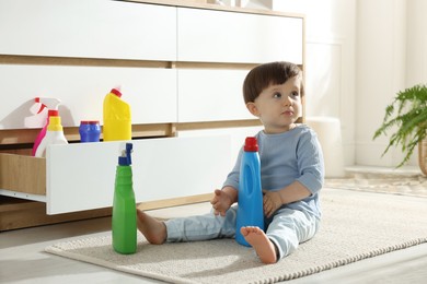 Photo of Little boy playing with bottles of detergents near cabinet at home. Child in danger