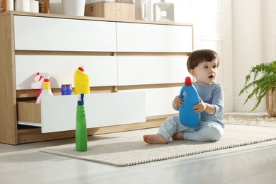 Photo of Little boy playing with bottles of detergents near cabinet at home. Child in danger