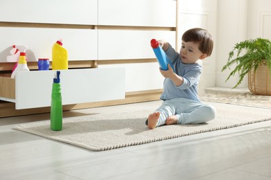 Photo of Little boy playing with bottles of detergents near cabinet at home. Child in danger