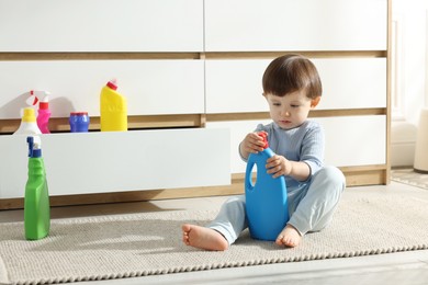 Photo of Little boy playing with bottles of detergents near cabinet at home. Child in danger