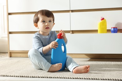 Photo of Little boy playing with bottles of detergents near cabinet at home. Child in danger