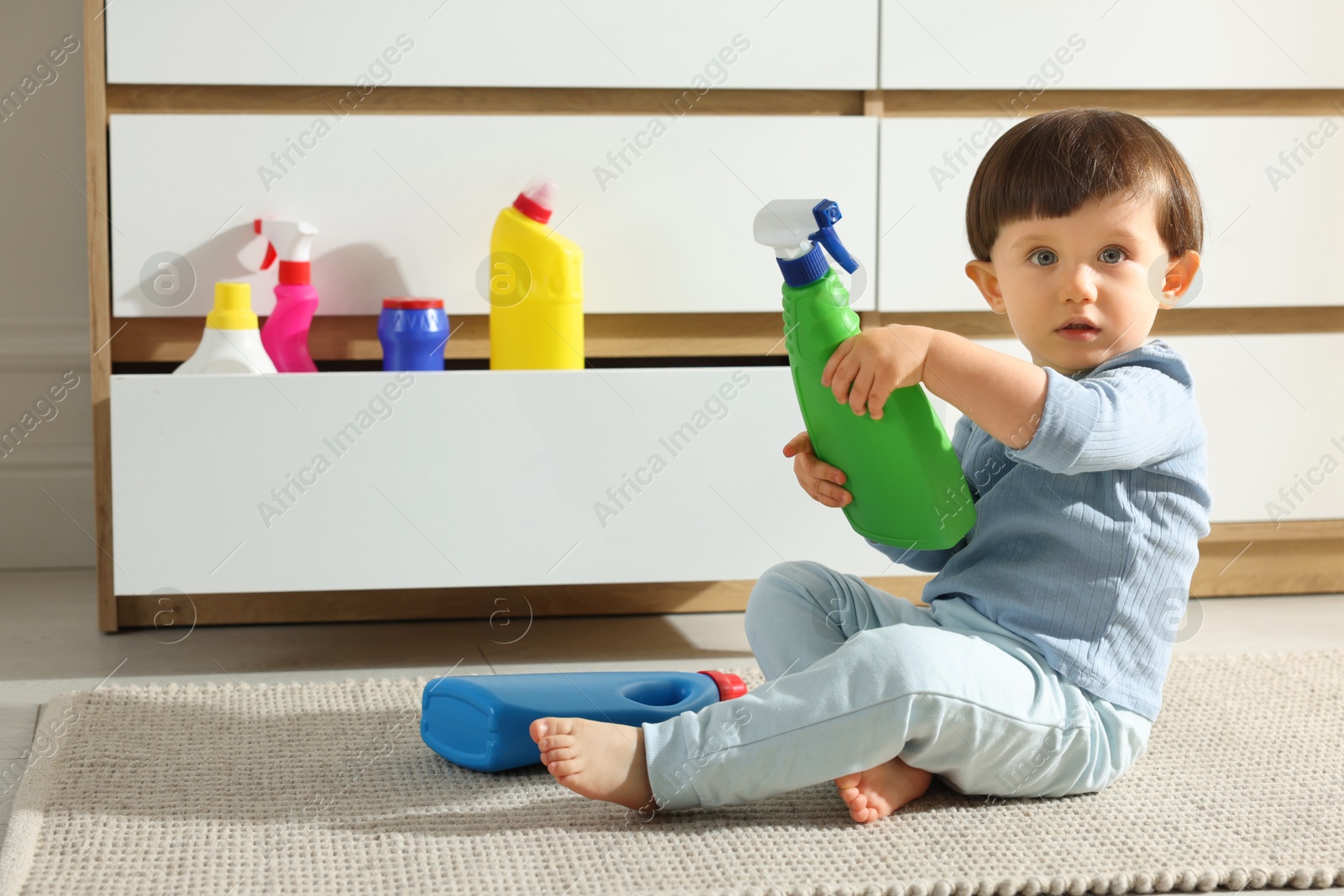 Photo of Little boy playing with bottles of detergents near cabinet at home. Child in danger