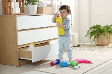 Photo of Little boy playing with bottles of detergents near cabinet at home. Child in danger