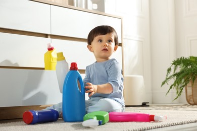 Photo of Little boy playing with bottles of detergents near cabinet at home. Child in danger