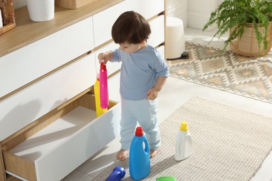 Photo of Little boy playing with bottles of detergents near cabinet at home. Child in danger