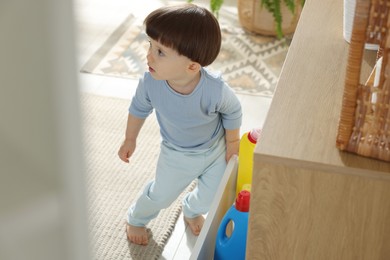 Photo of Little boy opening drawer with bottles of detergents at home. Child in danger