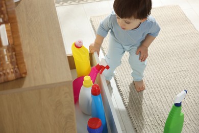 Photo of Little boy opening drawer with bottles of detergents at home. Child in danger