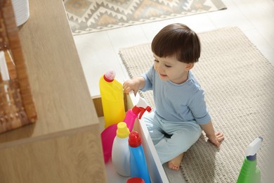 Photo of Little boy opening drawer with bottles of detergents at home. Child in danger