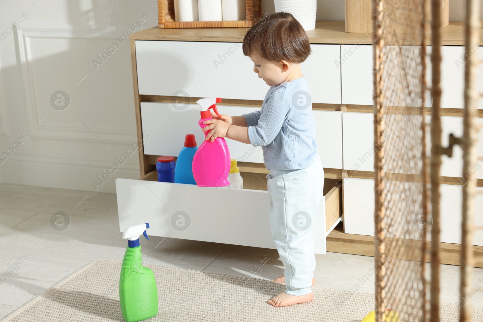 Photo of Little boy playing with bottle of detergent near cabinet at home. Child in danger