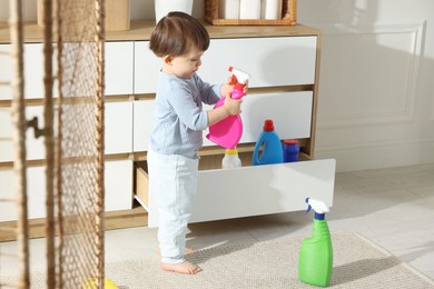 Photo of Little boy playing with bottle of detergent near cabinet at home. Child in danger