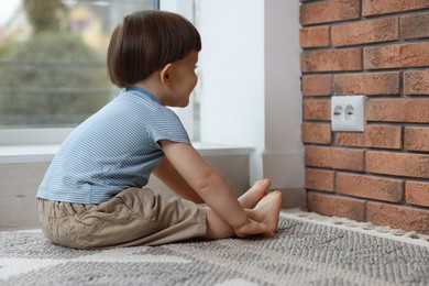 Photo of Little boy sitting near electrical socket at home. Child in danger