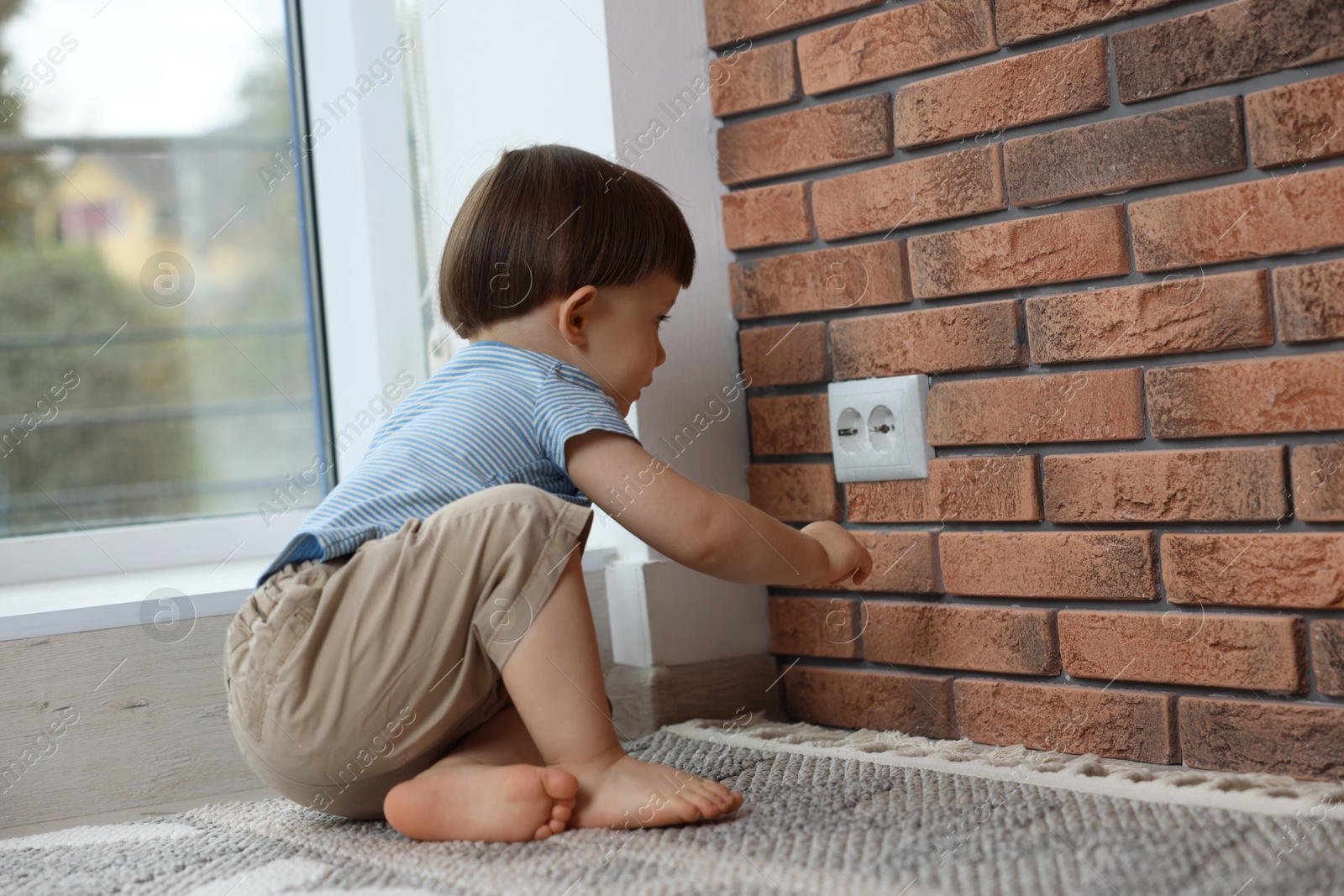 Photo of Little boy playing with electrical socket at home. Child in danger