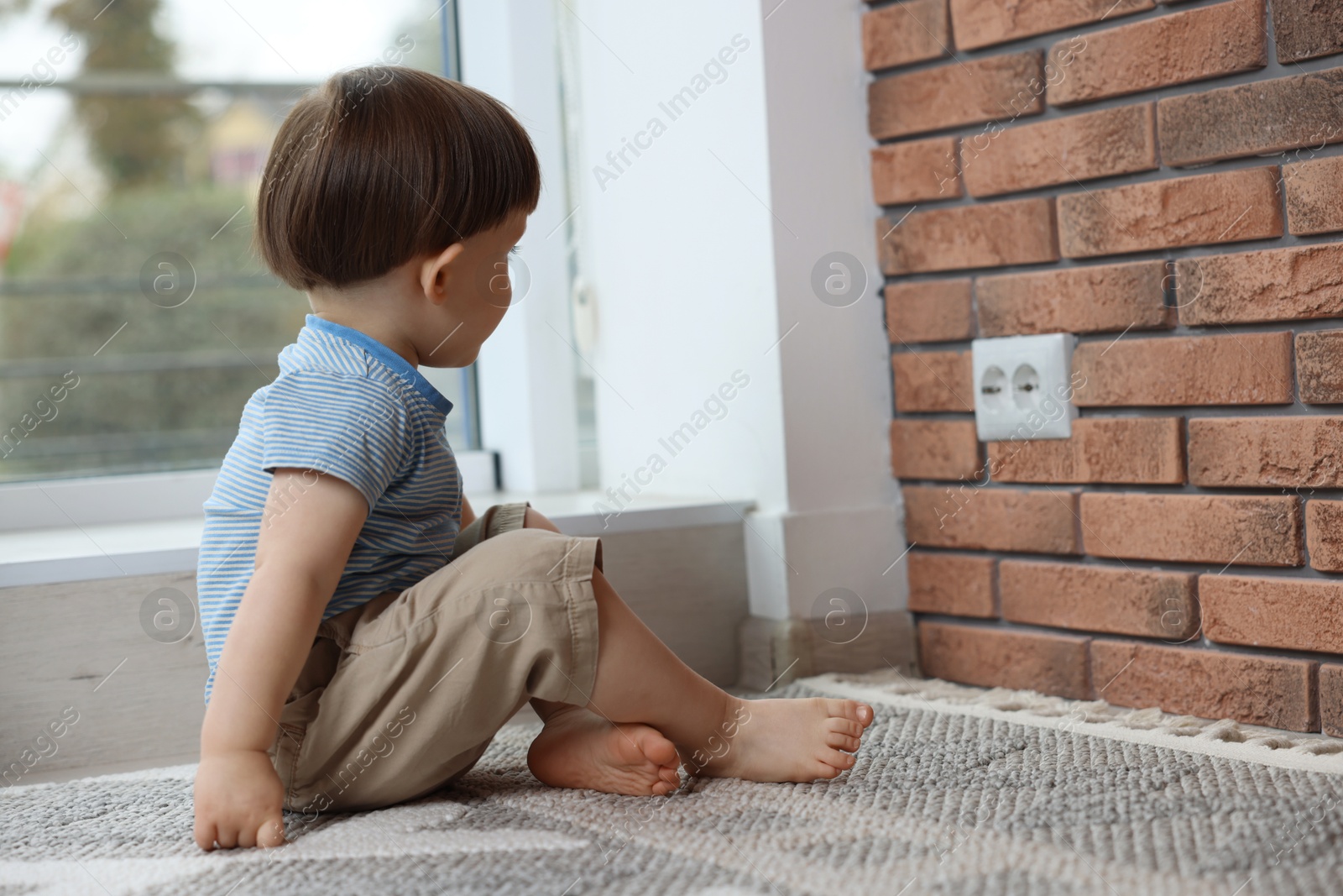 Photo of Little boy sitting near electrical socket at home. Child in danger