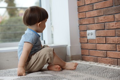 Photo of Little boy sitting near electrical socket at home. Child in danger