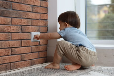 Photo of Little boy playing with electrical socket at home. Child in danger