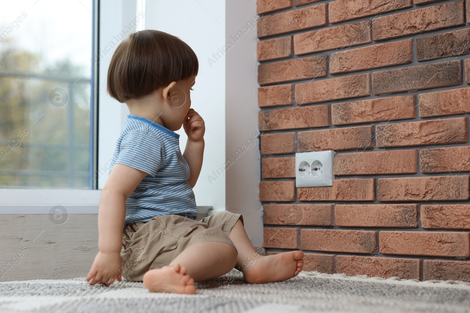 Photo of Little boy sitting near electrical socket at home. Child in danger