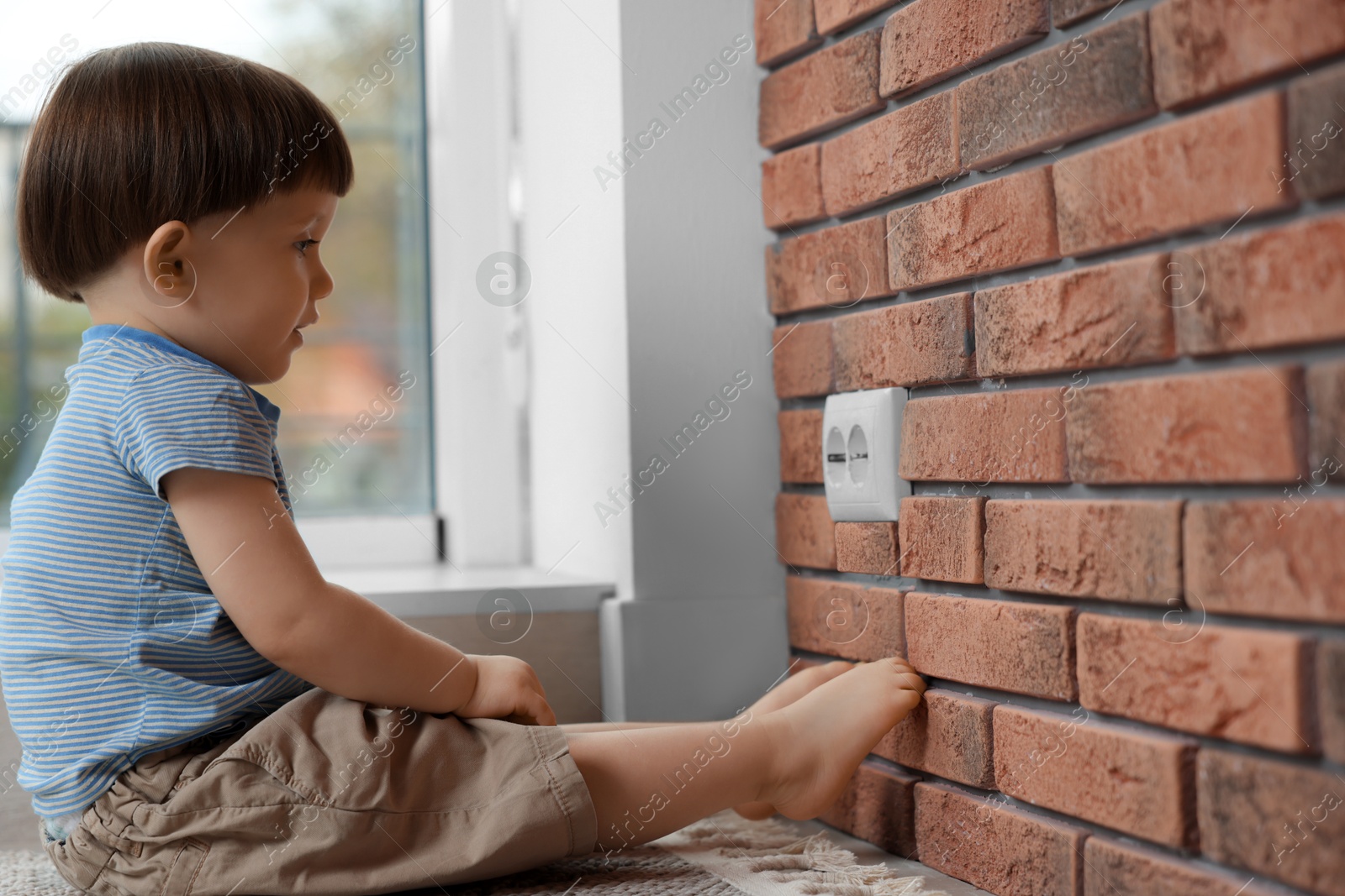 Photo of Little boy sitting near electrical socket at home. Child in danger