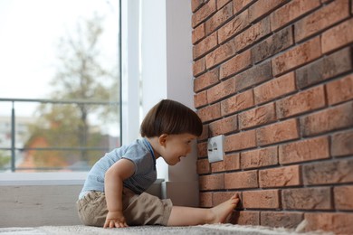 Photo of Little boy sitting near electrical socket at home. Child in danger