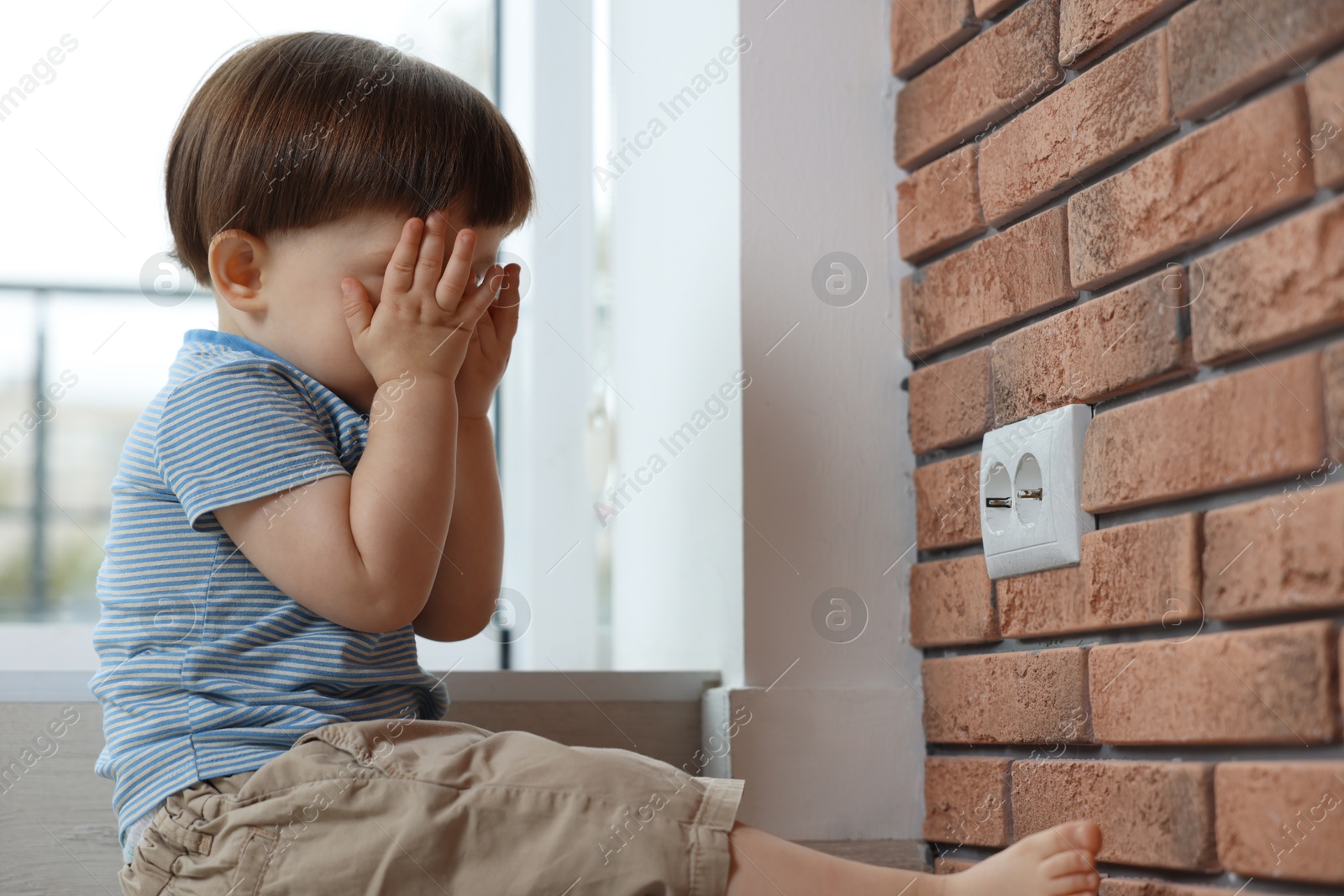 Photo of Little boy sitting near electrical socket at home. Child in danger