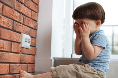 Photo of Little boy sitting near electrical socket at home. Child in danger