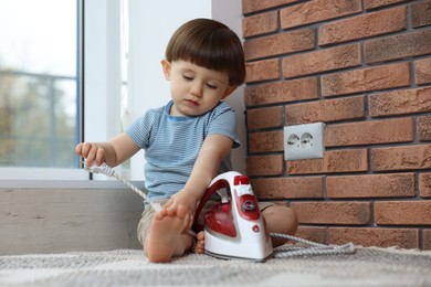 Photo of Little boy playing with iron plug near electrical socket at home. Child in danger