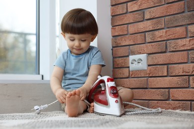 Photo of Little boy playing with iron plug near electrical socket at home. Child in danger