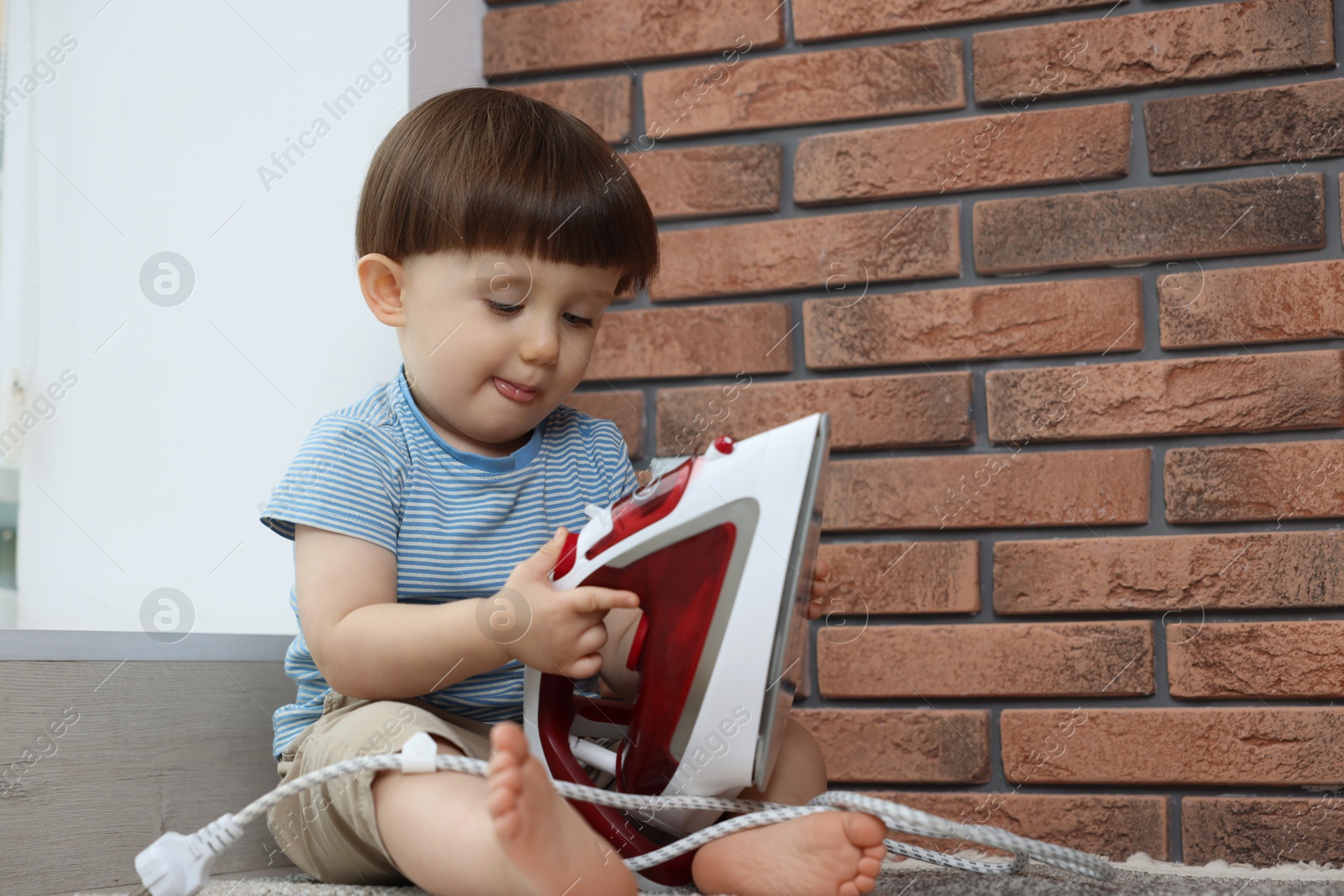 Photo of Little boy playing with iron at home. Child in danger