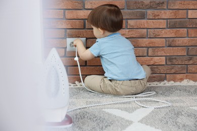 Photo of Little boy playing with iron plug and electrical socket at home, back view. Child in danger