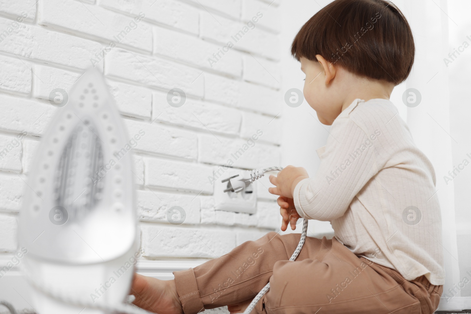 Photo of Little boy playing with iron plug and electrical socket at home. Child in danger