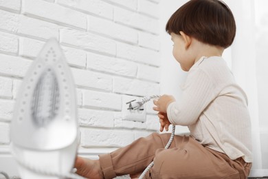 Photo of Little boy playing with iron plug and electrical socket at home. Child in danger