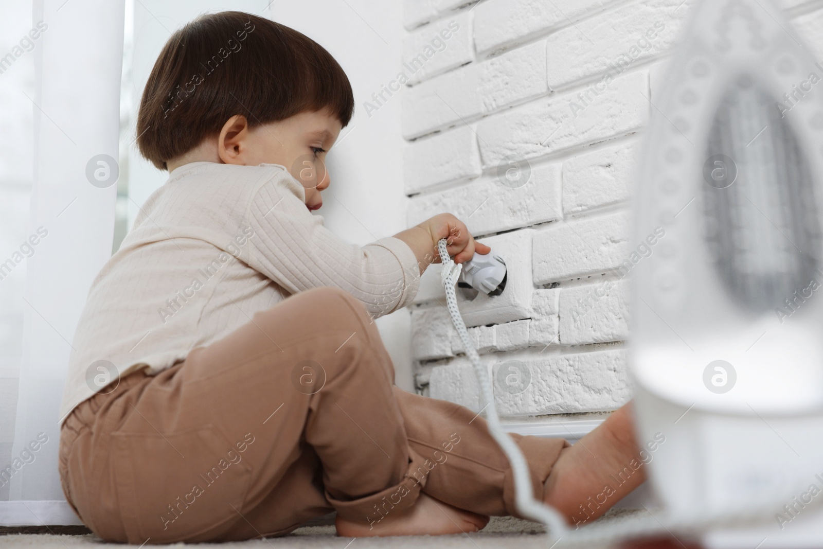 Photo of Little boy playing with iron plug and electrical socket at home. Child in danger