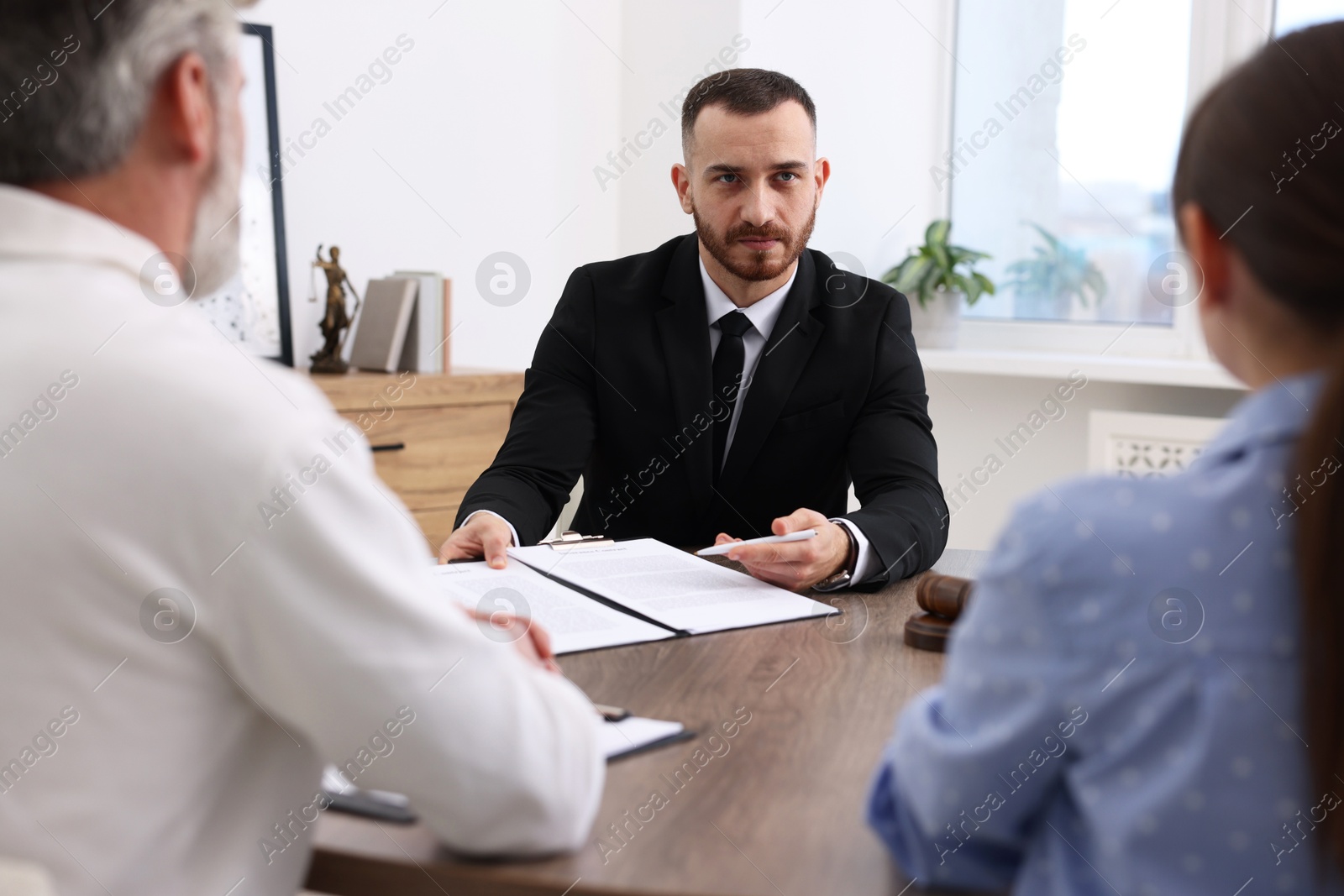 Photo of Man and woman having meeting with professional notary at wooden desk indoors