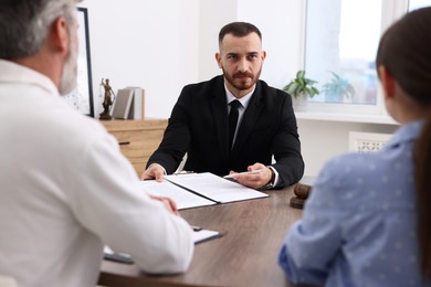 Man and woman having meeting with professional notary at wooden desk indoors