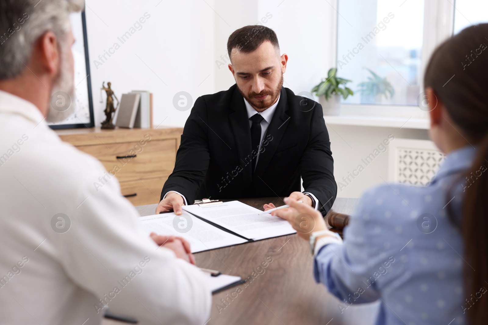 Photo of Man and woman having meeting with professional notary at wooden desk indoors