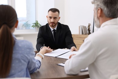 Photo of Man and woman having meeting with professional notary at wooden desk indoors