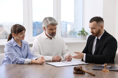 Photo of Clients signing notarial paperwork during meeting with lawyer at wooden desk indoors