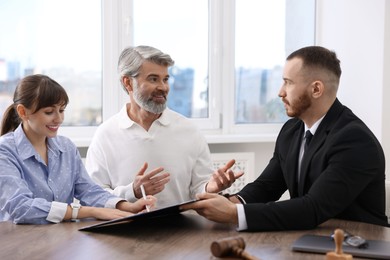 Clients signing notarial paperwork during meeting with lawyer at wooden desk indoors