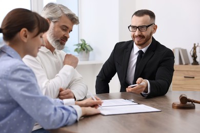 Clients signing notarial paperwork during meeting with lawyer at wooden desk indoors