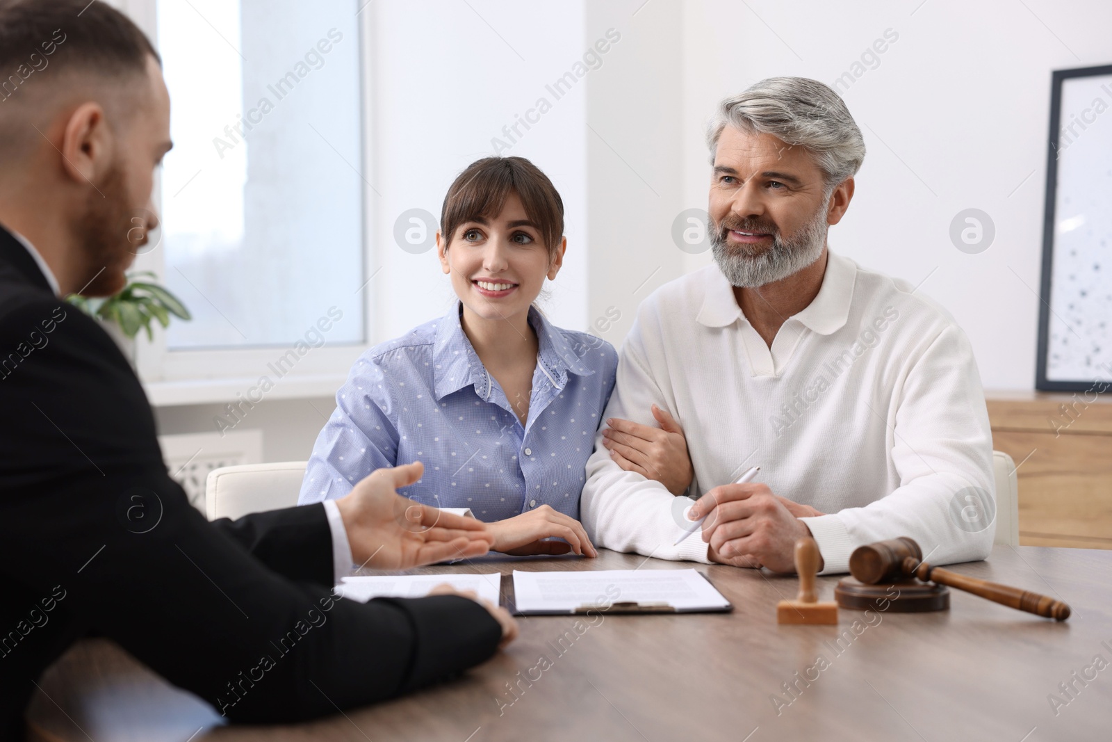 Photo of Couple having meeting with professional notary at wooden desk indoors