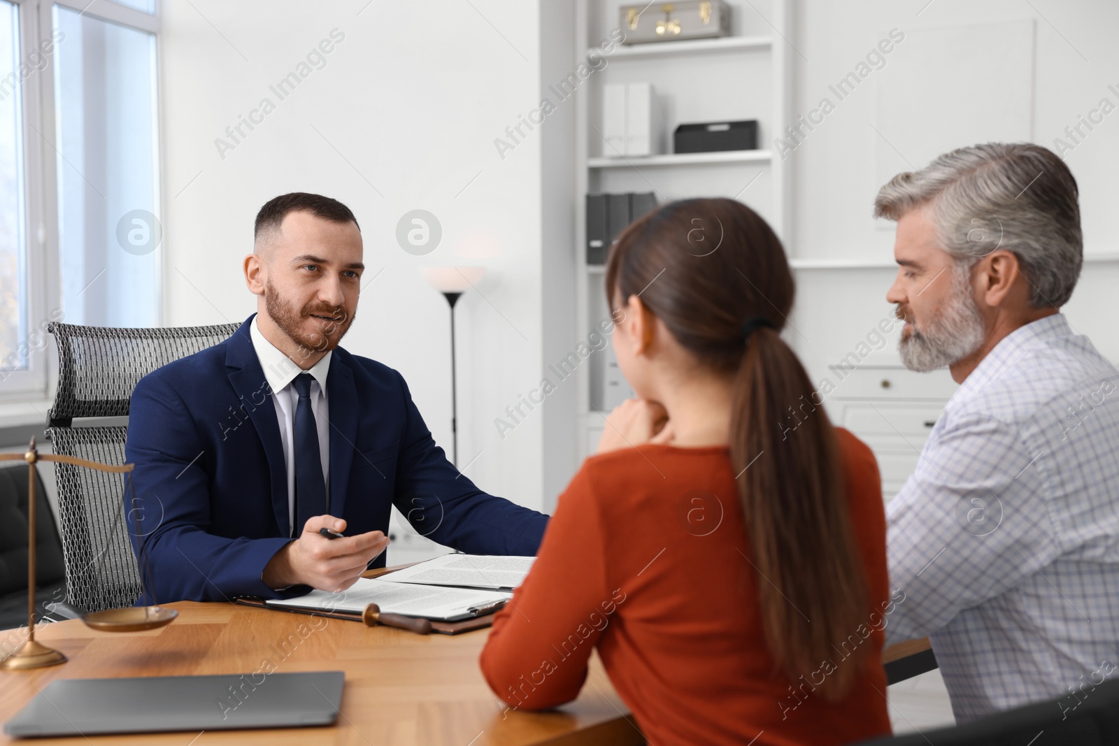 Photo of Couple having meeting with professional notary at wooden desk indoors