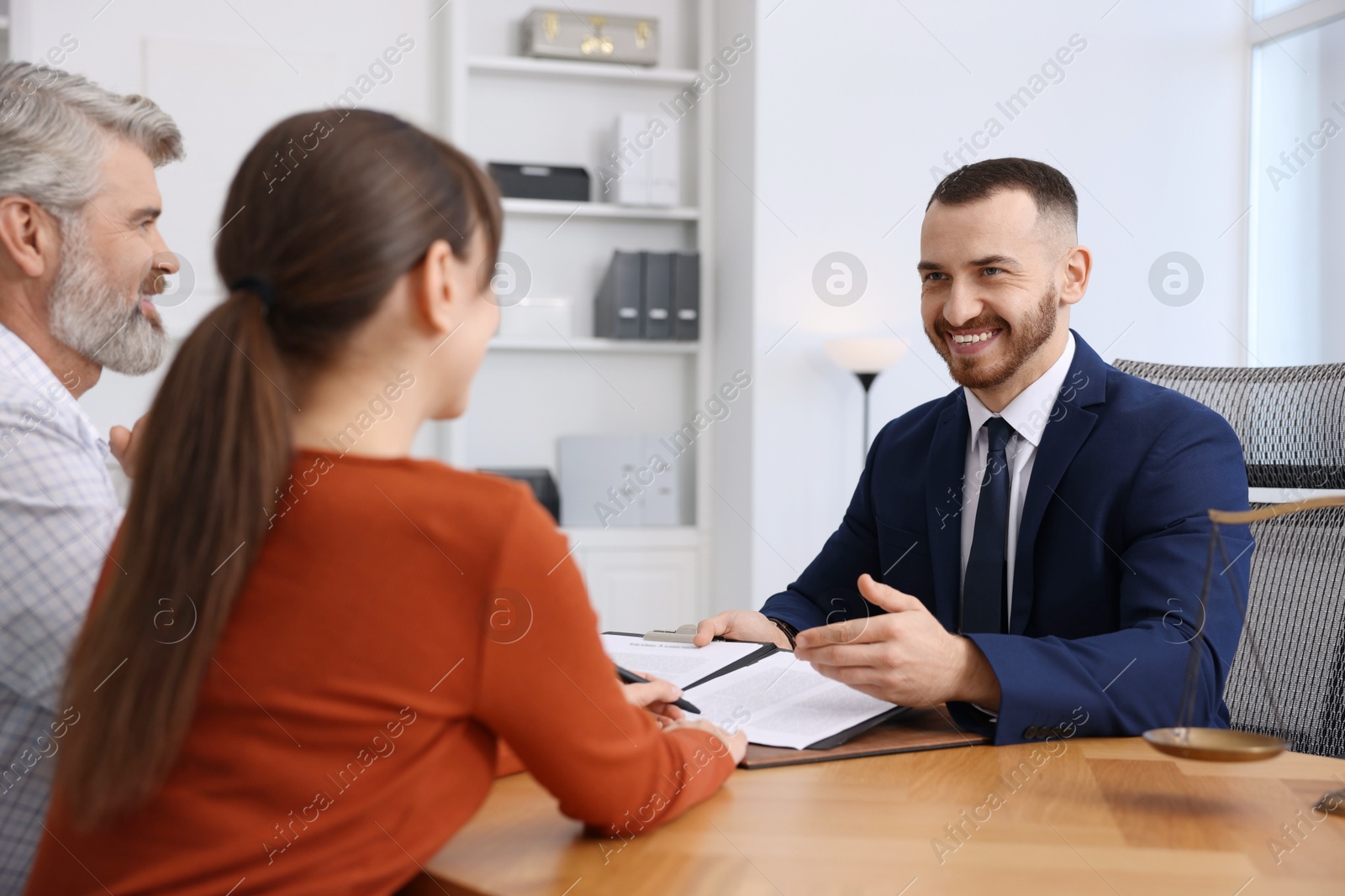 Photo of Couple having meeting with professional notary at wooden desk indoors