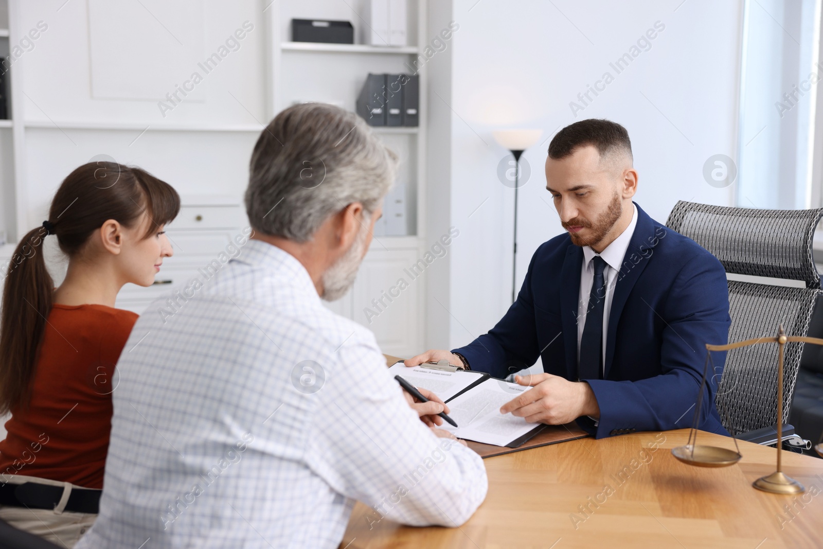 Photo of Clients signing notarial paperwork during meeting with lawyer at wooden desk indoors