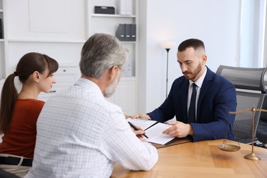 Clients signing notarial paperwork during meeting with lawyer at wooden desk indoors