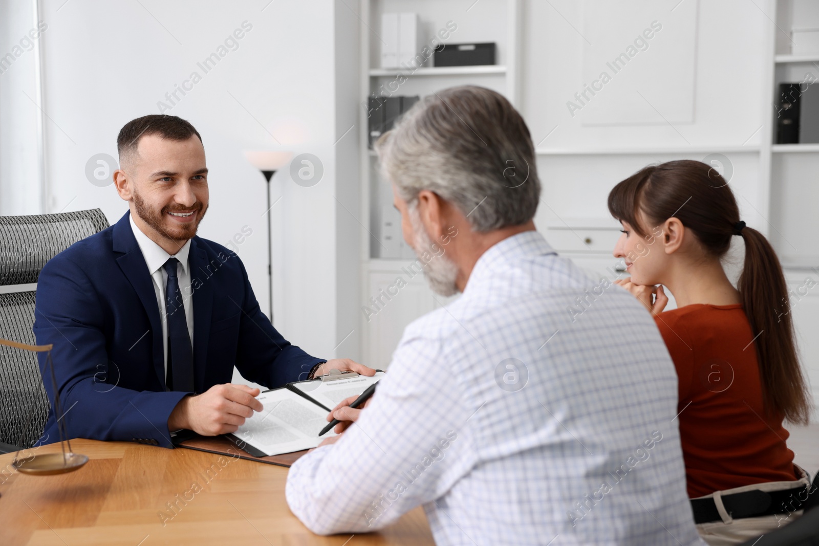 Photo of Clients signing notarial paperwork during meeting with lawyer at wooden desk indoors