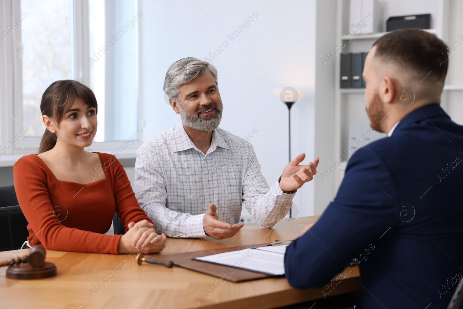 Photo of Couple having meeting with professional notary at wooden desk indoors